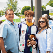 Master's student Jason Valdez wearing regalia, standing with his parents